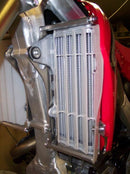 Close-up of the Radiator Frame by Emperor Racing, featuring metal and plastic components with hoses and a side tank. The metal sports an "Emperor Racing" logo.