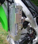 A close-up of a motorcycle radiator featuring the Emperor Racing Radiator Guard. It's encased in a red and white fairing, with visible engine and exhaust pipes below. Parts of the frame and a rear-view mirror are also seen.