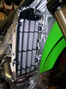 Close-up of the Radiator Frame by Emperor Racing, featuring metal and plastic components with hoses and a side tank. The metal sports an "Emperor Racing" logo.