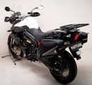 A blue adventure motorcycle, equipped with dual exhausts and off-road tires, is parked on a stand against a white background. It features a windshield and a black rear-mounted Tough-Rack by Ventura for luggage.