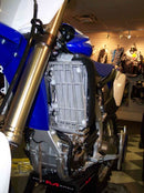 Close-up of the Radiator Frame by Emperor Racing, featuring metal and plastic components with hoses and a side tank. The metal sports an "Emperor Racing" logo.