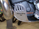 Close-up of the Emperor Racing Heavy Duty Skid Plate with a scorpion design, made from durable aluminum and installed under the engine. Its polished surface and visible bolts contrast with a blurred wooden fence background—ideal for off-road enthusiasts.