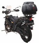 A blue adventure motorcycle, equipped with dual exhausts and off-road tires, is parked on a stand against a white background. It features a windshield and a black rear-mounted Tough-Rack by Ventura for luggage.