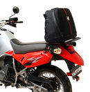 A blue adventure motorcycle, equipped with dual exhausts and off-road tires, is parked on a stand against a white background. It features a windshield and a black rear-mounted Tough-Rack by Ventura for luggage.