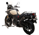 A blue adventure motorcycle, equipped with dual exhausts and off-road tires, is parked on a stand against a white background. It features a windshield and a black rear-mounted Tough-Rack by Ventura for luggage.