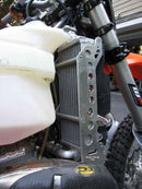 Close-up of the Radiator Frame by Emperor Racing, featuring metal and plastic components with hoses and a side tank. The metal sports an "Emperor Racing" logo.