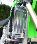 A close-up of a motorcycle radiator featuring the Emperor Racing Radiator Guard. It's encased in a red and white fairing, with visible engine and exhaust pipes below. Parts of the frame and a rear-view mirror are also seen.