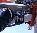 Close-up of a motorcycle's rear suspension showcasing Emperor Racing's Linkage Skid Plate. Visible components include the chain, sprocket, footpeg, and brake system. The tire has deep treads, and high-grade aluminum accents complement the metallic chassis with red and black highlights.