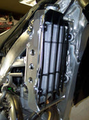 Close-up of the Radiator Frame by Emperor Racing, featuring metal and plastic components with hoses and a side tank. The metal sports an "Emperor Racing" logo.