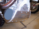 Close-up of the Emperor Racing Heavy Duty Skid Plate with a scorpion design, made from durable aluminum and installed under the engine. Its polished surface and visible bolts contrast with a blurred wooden fence background—ideal for off-road enthusiasts.