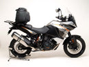 A blue adventure motorcycle, equipped with dual exhausts and off-road tires, is parked on a stand against a white background. It features a windshield and a black rear-mounted Tough-Rack by Ventura for luggage.