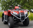 A Ventura Kymco MXU 400 (21 ->) ATV with large off-road tires and a silver bull bar is parked on pavement near green bushes and trees.