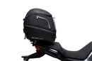 The Ventura EVO-12 Bike-Pack Kit for Moto Guzzi V100, V100S Mandello (22 - >) includes a black EVO-12 pack, a black Evo-Rack or Adjustable Pack-Rack mounted on the motorcycle, and an image of a labeled L-bracket with hardware.