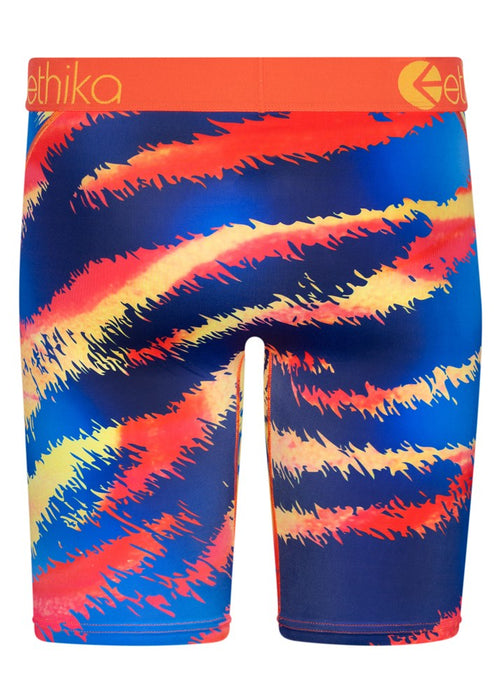 The image features the Ethika III Tiger Staple men's boxer briefs with a bold, graphic design showcasing a vibrant, fierce tiger face in shades of blue, orange, yellow, and red. The high-quality orange jacquard waistband prominently displays the brand name "ethika" in white letters.