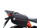 Ventura's EVO-12 Bike-Pack Kit image features a striking black EVO-12 pack with vibrant orange accents, an EVO-Rack gracefully fitted on a Suzuki DL 1050 V-Strom XT bike, and an L-Bracket with screws. The Adjustable Pack-Rack is designed to enhance your biking experience.