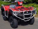 A Ventura Suzuki LT-A 750XP in red is parked on a road, featuring a sturdy front bumper and large knobby tires. With durable bull bars, it's primed for rugged adventures. Green shrubs and foliage provide a lush backdrop to this powerful machine.