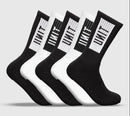 Five pairs of Unit Box Bamboo Hi Lux socks—alternating black and white—stand upright, each with a vertical black-and-white “UNIT” logo on the side, crafted from an anti-bacterial bamboo blend against a plain light gray background.