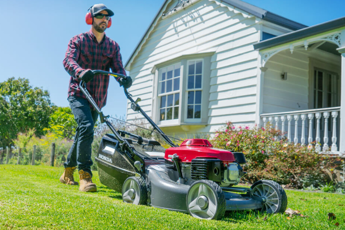 Man mowing a lawn with a Honda lawn mower in front of a house.