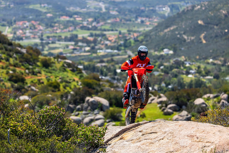 The 2025 Honda CRF250RX is a red off-road bike featuring a sturdy frame, knobby tires, and a black seat. It includes front and rear suspension with visible springs and displays prominent "Honda" branding on the side. The motorcycle is presented against a plain backdrop.