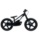 A STACYC 18eDRIVE Brushless - Electric Balance Bike in black, featuring a sleek design, is displayed outdoors on a paved surface. It is powered by a 36 Volt BRUSHLESS motor and is resting on a stand with a lush, green landscape in the background.