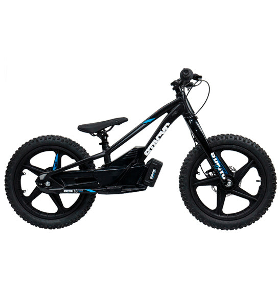 A STACYC 18eDRIVE Brushless - Electric Balance Bike in black, featuring a sleek design, is displayed outdoors on a paved surface. It is powered by a 36 Volt BRUSHLESS motor and is resting on a stand with a lush, green landscape in the background.