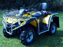 A Ventura Can-Am Outlander MAX DPS 570 (2017) ATV, yellow with black tires, silver bull-bars, a tow-ball, padded seat and backrest, is parked on grass with shrubbery and trees in the background.