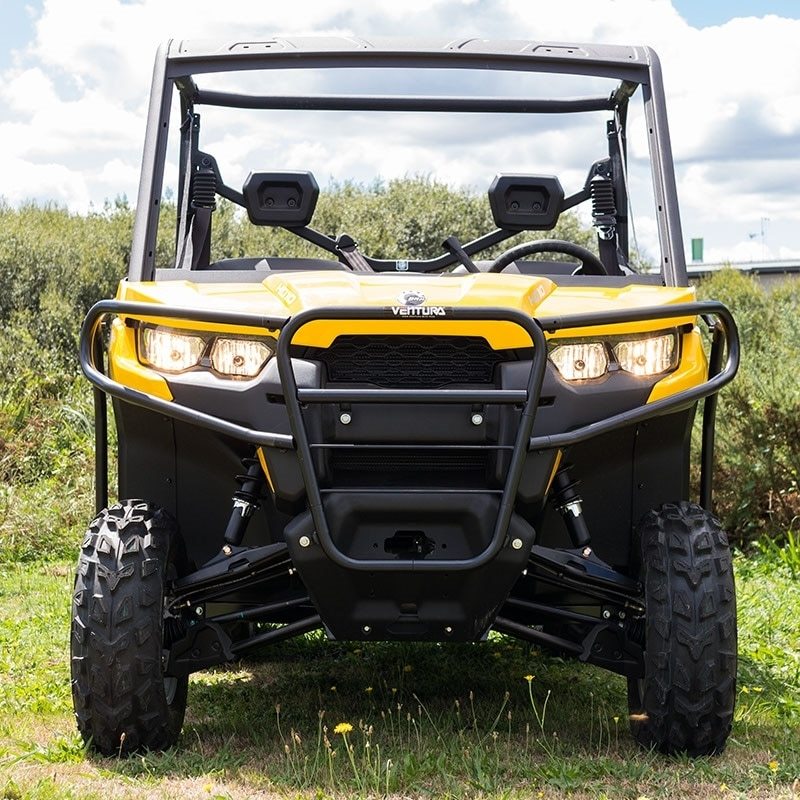 A Ventura Can-Am ATV Defender HD10 (16-17), painted yellow and black, is parked on grassy terrain. This off-road utility vehicle features rugged tires, a sturdy bull-bar, a protective front grille, mud flaps, and two side mirrors against a backdrop of greenery and a partly cloudy sky.