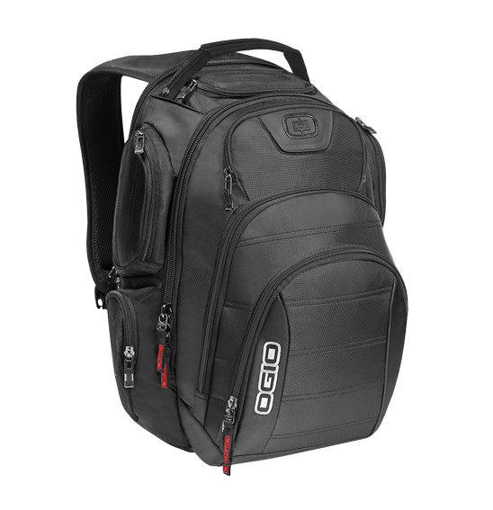 The Ogio REV Laptop Backpack in black is shown, showcasing its sleek design and multiple compartments. Featuring ergonomic shoulder straps, it is packed with various items including a laptop, tablet, water bottle, headphones, smartphone, and other electronics—all neatly organized in their respective pockets. It also includes a Tech Vault pocket for added protection.