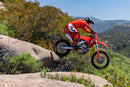 The 2025 Honda CRF250RX is a red off-road bike featuring a sturdy frame, knobby tires, and a black seat. It includes front and rear suspension with visible springs and displays prominent "Honda" branding on the side. The motorcycle is presented against a plain backdrop.