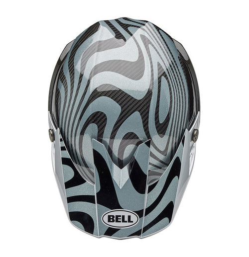 The Bell MOTO-10 SPHERICAL Cortex Gloss Silver/Grey helmet showcases a sleek, modern motocross design with a gray and black swirling pattern. It features angular lines, a visor peak, and incorporates MIPS technology for enhanced safety. The brand name "BELL" is prominently displayed on the side.