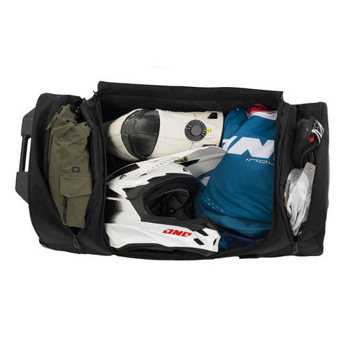 The OGIO CRAWLER Gear Bag - Black is a large wheeled gear bag featuring off-road wheels, a retractable handle, side straps, and a spacious main compartment. It is shown upright and slightly angled to the right.