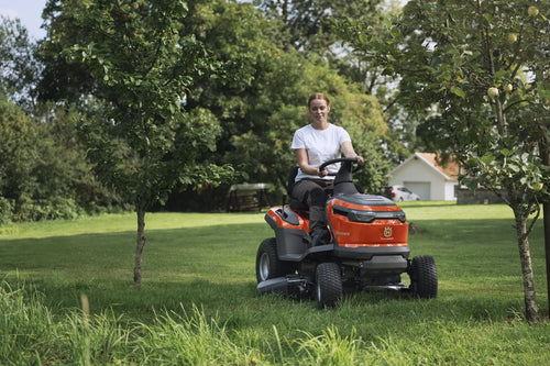 The Husqvarna Battery TS 100i Tractor, in orange with a black seat and steering wheel, offers ergonomic comfort and features robust wheels with visible blade housing. The brand logo is prominently displayed on the side, ensuring efficient mowing with every use.
