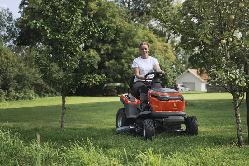The Husqvarna Battery TS 100i Tractor, in orange with a black seat and steering wheel, offers ergonomic comfort and features robust wheels with visible blade housing. The brand logo is prominently displayed on the side, ensuring efficient mowing with every use.