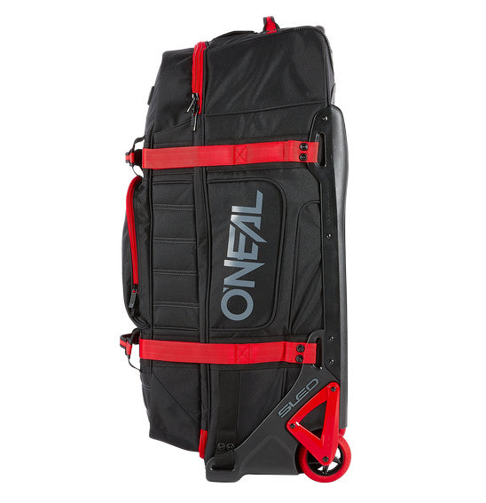 A large, black and red O'NEAL x OGIO RIG 9800 Gear Bag by ONEAL is standing upright. This travel bag is designed with multiple compartments, zippers, and adjustable straps. The SLED system ensures extra durability, while the OGIO logo is prominently displayed on the front alongside the text "ENJOY THE RIDE.