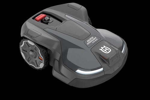 The Husqvarna Automower 430X NERA is a sleek, grey robotic lawn mower featuring two large wheels at the rear and two smaller wheels at the front. It boasts a red stop button on top, LED headlights, and proudly displays the Husqvarna logo on the front. With its modern design, this mower is equipped with object avoidance technology and can be conveniently controlled via the Automower Connect app.