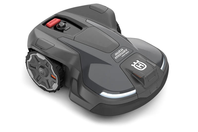 The Husqvarna Automower 430X NERA is a sleek, grey robotic lawn mower featuring two large wheels at the rear and two smaller wheels at the front. It boasts a red stop button on top, LED headlights, and proudly displays the Husqvarna logo on the front. With its modern design, this mower is equipped with object avoidance technology and can be conveniently controlled via the Automower Connect app.