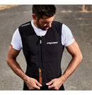 A man wearing the Ixon IX-AIRBAG U03 Airbag Vest over a white shirt adjusts the front zipper. The vest, showcasing logos such as "Ixon" and "In&motion airbag," provides advanced motorcycle protection. The background features an outdoor paved area.