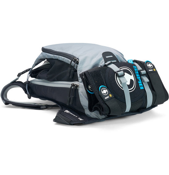 A neatly arranged display of USWE's Patriot 15L MTB Protector Pack highlights its gray backpack with open compartments, black sleek padding, and straps with blue branding. Featuring the CE-certified SAS-TEC protection and an NDM 4-point harness system, it's engineered for high-performance outdoor activities.