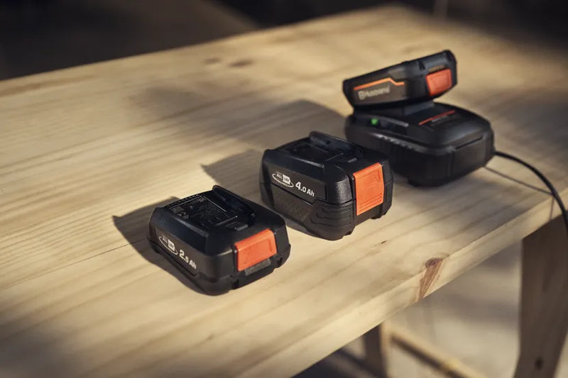 A compact Husqvarna Aspire™ P4A 18-B45 Battery with a black and orange exterior. Ideal for forestry or lawns, the battery features a push button mechanism on the orange section and branding on the side. A red badge indicating "POWER FOR ALL 18V" is seen at the bottom right corner.