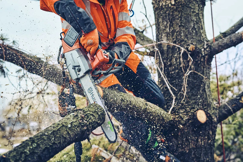 The Husqvarna T542i XP Battery Chainsaw (Skin Only) features an eye-catching orange and black body, a sturdy metal chain bar with the "Husqvarna" brand name displayed on it, a grip handle, and various adjustment controls against a transparent background.