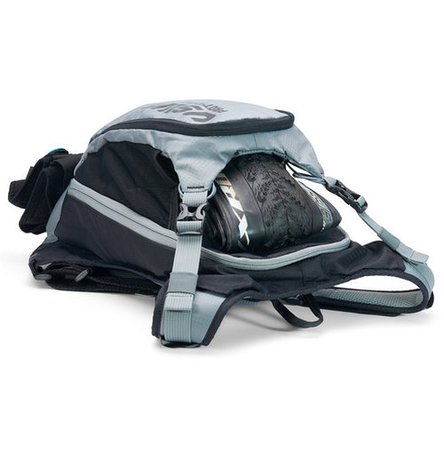 A neatly arranged display of USWE's Patriot 15L MTB Protector Pack highlights its gray backpack with open compartments, black sleek padding, and straps with blue branding. Featuring the CE-certified SAS-TEC protection and an NDM 4-point harness system, it's engineered for high-performance outdoor activities.