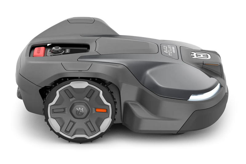 The Husqvarna Automower 430X NERA is a sleek, grey robotic lawn mower featuring two large wheels at the rear and two smaller wheels at the front. It boasts a red stop button on top, LED headlights, and proudly displays the Husqvarna logo on the front. With its modern design, this mower is equipped with object avoidance technology and can be conveniently controlled via the Automower Connect app.