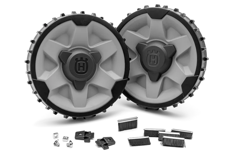 The Husqvarna Automower® Rough Terrain Kit by Husqvarna is displayed, featuring two rugged, circular robotic mower wheels with black and white treads. These treaded wheels have thick patterns suitable for rough terrain, providing excellent traction with accents in orange and gray, accompanied by a set of five small, black bristle brushes.