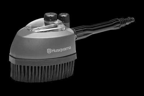 The Husqvarna Rotating Brush Kit is a handheld grey brush attachment for a cleaning device featuring black bristles, a transparent plastic cover on top, and a black handle with visible grooves. It proudly displays the brand name "Husqvarna" on the side.