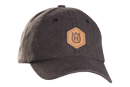 Introducing the Husqvarna Xplorer Cap in granite, featuring a tan leather patch on the front with a circular emblem displaying an "H" at its center. This cap boasts textured fabric and detailed stitching, promising a perfect fit thanks to its adjustable leather band at the back.