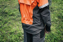 The Husqvarna Technical Forest Jacket is an orange and black outdoor jacket with a high collar and multiple panels. Made from four-way stretch polyester, it features a prominent white Husqvarna logo on the right chest and arm. The jacket includes ventilation openings and reflective strips for added visibility, making it sleek, functional, and ideal for forestry work.
