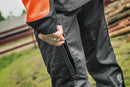 A pair of **Husqvarna Classic Waist trousers** designed for chainsaw use, featuring chainsaw protection. The trousers are primarily orange at the top and grey at the bottom, with reinforced black patches on the knees and lower legs for added durability. Perfect workwear twill for demanding tasks.