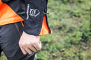 The Husqvarna Technical Forest Jacket is an orange and black outdoor jacket with a high collar and multiple panels. Made from four-way stretch polyester, it features a prominent white Husqvarna logo on the right chest and arm. The jacket includes ventilation openings and reflective strips for added visibility, making it sleek, functional, and ideal for forestry work.