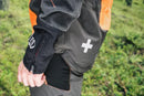 The Husqvarna Technical Forest Jacket is an orange and black outdoor jacket with a high collar and multiple panels. Made from four-way stretch polyester, it features a prominent white Husqvarna logo on the right chest and arm. The jacket includes ventilation openings and reflective strips for added visibility, making it sleek, functional, and ideal for forestry work.