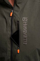 The Husqvarna Xplorer Shell Jacket - Forest Green is showcased on an invisible mannequin. Crafted from water-resistant shell material, this dark green jacket features a hood, zippered chest and side pockets, and eye-catching orange accents. It also proudly displays the Husqvarna logo stitched on both the chest and arm, while adjustable ventilation provides added comfort.